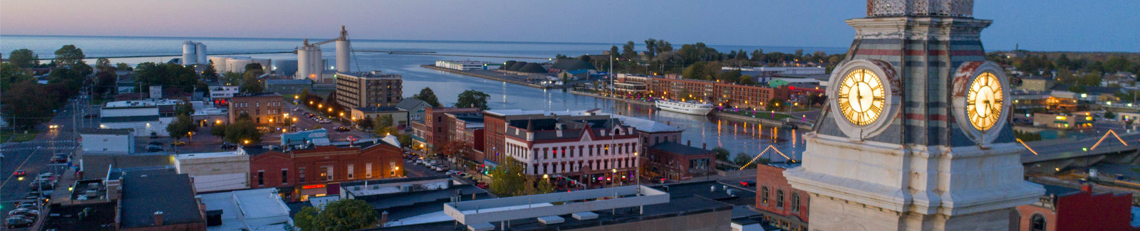 Aerial view of Oswego City Hall at sunset in the foreground, with the view of the Oswego River, harbor/pier, and horizon in the background.